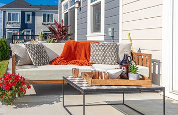 A grey couch with a pillow and a blanket on it is on a patio.